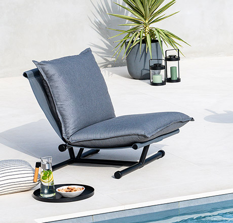 niedriger Lounge-Sessel mit Stahlgestell, Sitzpolster in Grau, neben einem Pool