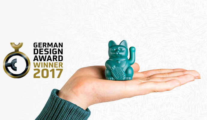 German Design Award Winner 2017, Hand mit petrolfarbiger kleiner Winkekatze