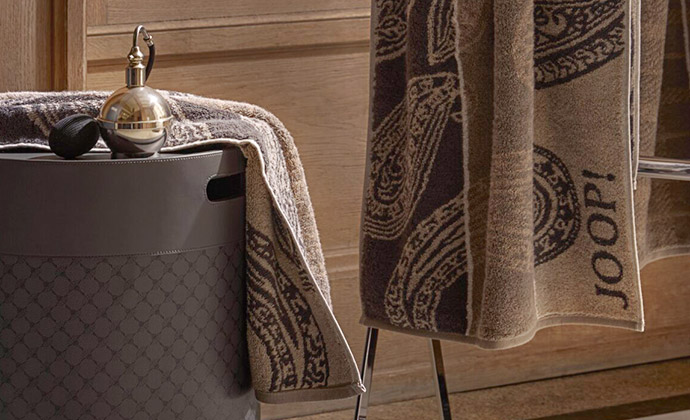 grauer Lederhocker mit Parfümflakon, 2 beige Handtücher mit Paisley-Muster und JOOP! Schriftzug