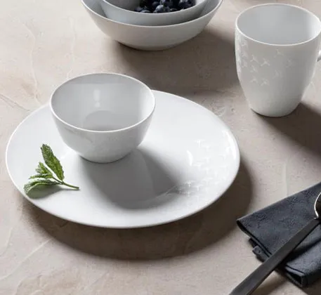 weißes Porzellan-Geschirr mit Cornflower-Muster auf beigem Tisch, schwarze Serviette und schwarzer Löffel 
