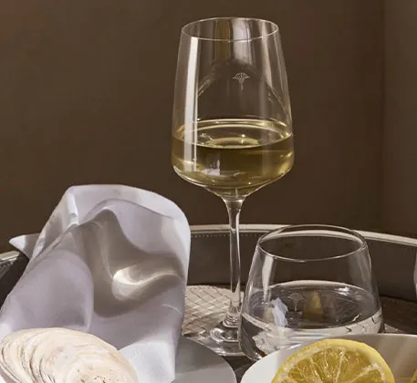 weiße Serviette mit Muschel, Weinglas mit Cornflower-Muster und Weißwein, Wasserglas , Zitrone in weißer Schale
