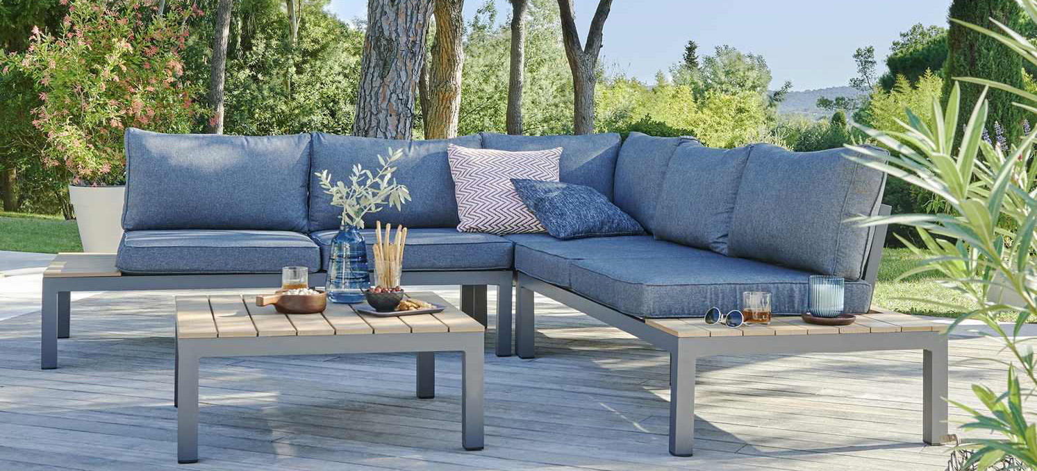 Terrasse mit Garten-Ecksofa und Tisch aus Alu und Holz - rechts seitlich und im Hintergrund Pflanzen, Bäume und Sträucher