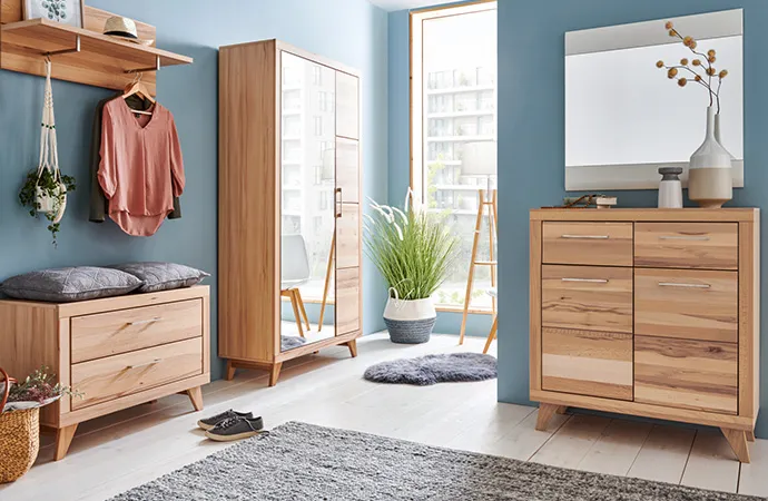 Flur mit Flurmöbeln aus Holz im Skandi-Stil, bestehend aus Gardeobenbank mit grauen Kissen, Garderobenschrank mit einer Spiegeltür, Kommode und Spiegel, Kleidung, Deko.
