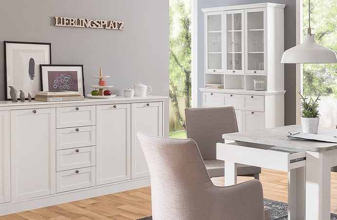 Weiße Möbelserie im Landhausstil mit Rahmenfronten, an der Wand Schriftzug "Lieblingsplatz"