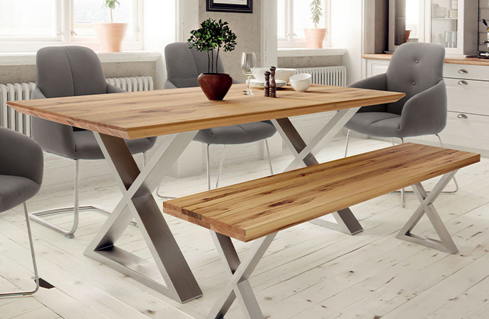 Essgruppe mit Esstisch mit Echtholz-Tischplatte und Metallgestell in X-Form und Bank mit Echtholz-Bankplatte und Metallgestell in X-Form - im Hintergrund graue Polsterstühle