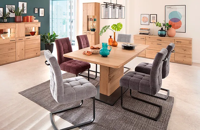 Esszimmer mit beleuchteten Holzmöbeln, bestehend aus Sideboard, Vitrine, Kommode, Esstisch, Polsterstühle in Hell- und Dunkelgrau, Lila mit Metallgestell.