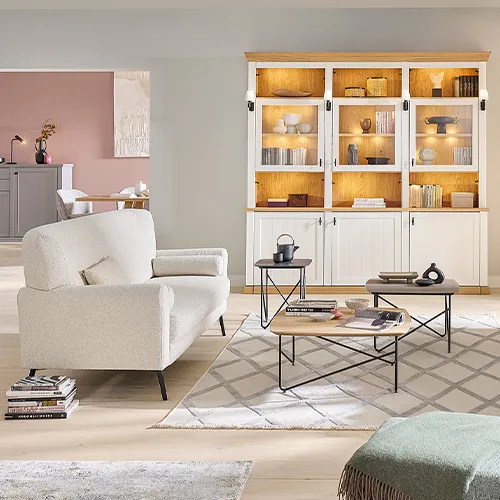 Wohnzimmer mit weißem Sofa, beleuchtetem Buffet im Landhausstil in Weiß und Holz, Couchtische, Deko
