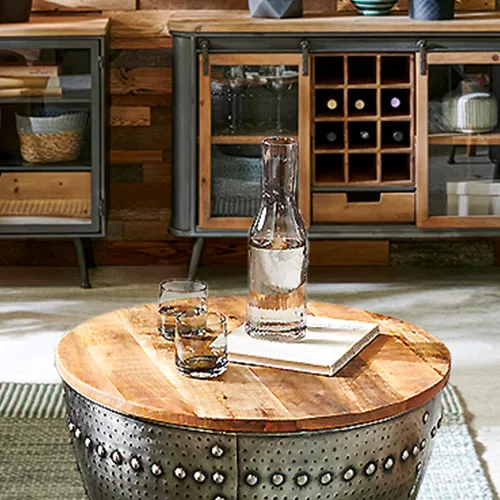 Industrial-Wohnzimmer mit braunem Sofa, 2 Kommoden und einem Lowboard in Holzoptik und grauem Metall, runder Couchtisch mit Holztischplatte und Metallgestell mit Nieten