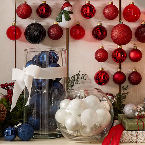 Weihnachtskugeln in Blau und Weiß in Glasvasen, rote Weihnachtskugeln an heller Holzwand aufgehängt