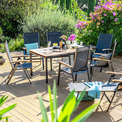 Holzterrasse im Grünen, Sitzgruppe mit Esstisch und 6 Stühlen in Schwarz und Holzoptik, Stühle mit Textil bespannt, passende Gartenliege daneben