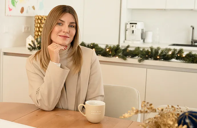 Frau auf beigem Sessel mit kleiner weißer Katze in der Hand