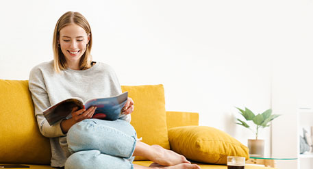 Frau sitzt auf Sofa und blättert in Zeitschrift