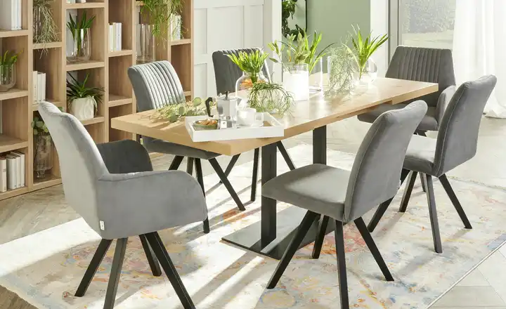 Sechs graue Stühle mit gesteppter Lehne und schwarzem Gestell an einem hellen Holztisch mit schwarzem Gestell