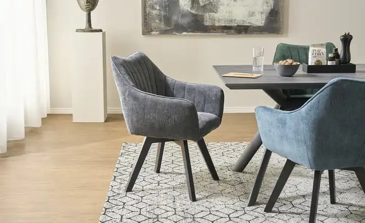 Sechs graue Stühle mit gesteppter Lehne und schwarzem Gestell an einem hellen Holztisch mit schwarzem Gestell