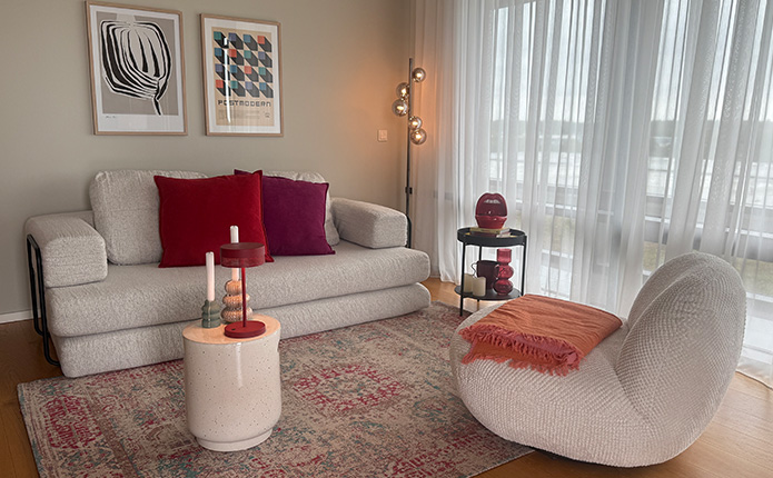 Sofa in Creme mit gemütlich passendem Sessel, roten Dekoaccessoires und modernem Stil