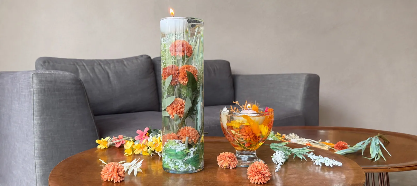 Hohe Vase und kleine Eisschale aus Glas mit Trockenblumen-Arrangements in herbstlichen Farbtönen unter Wasser mit Schwimmkerzen