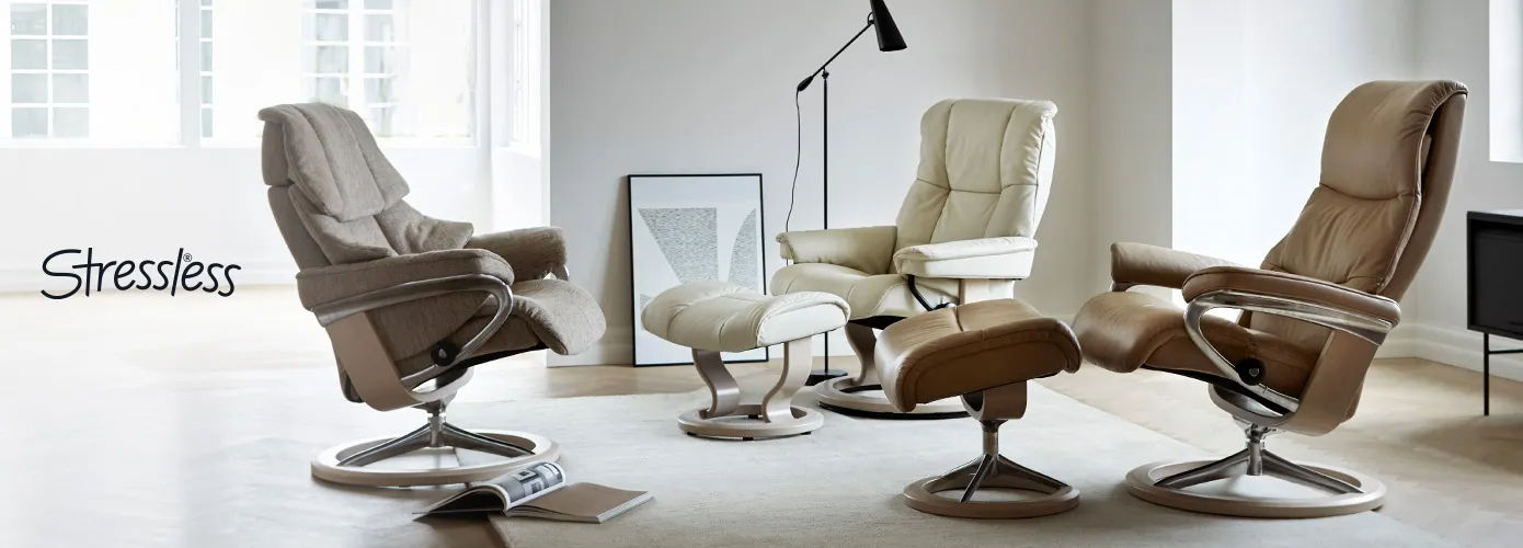 Stressless. Hellbrauner Sessel mit Holz-Metallgestell, weißer Sessel mit Holzgestell, cognacbrauner Sessel mit Holz-Chrom-Gestell, Deko in einem Wohnzimmer