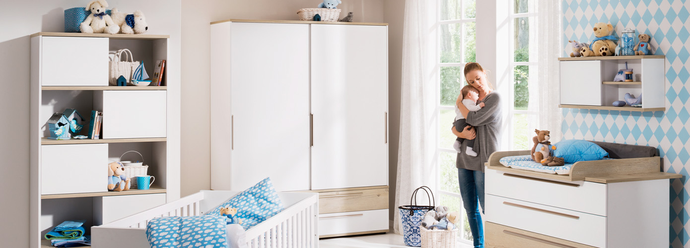 Babyzimmer mit Frau und Baby sowie Babymöbeln in Weiß und Holzoptik, bestehend aus Regal, Babybett, Schrank, Wickelkommode und Wandregal, Spielzeug und Deko