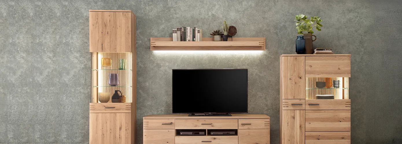 Wohnkombination aus Holz mit Beleuchtung, bestehend aus Vitrine, Wandboard, Lowboard und Highboard, Deko und TV vor grauer Betonwand