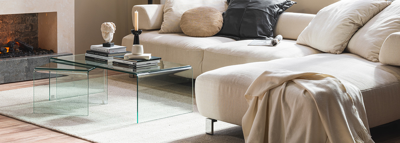 Beiger Teppich vor einem cremefarbenen Sofa mit zwei gläsernen Beistelltischen darauf