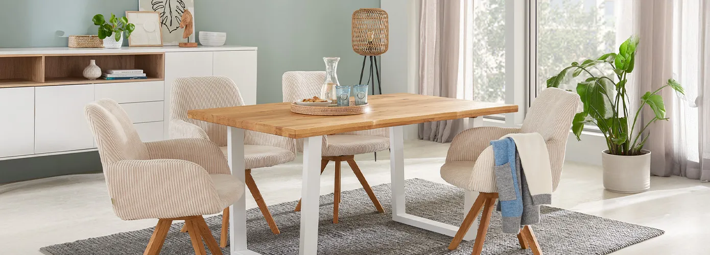 Esszimmer mit Esstisch aus Holz mit U-Gestell aus weißem Metall, 4 Polstersessel aus beigem Cord mit Holzgestell, grauer Teppich, weißes Sideboard, Deko. 